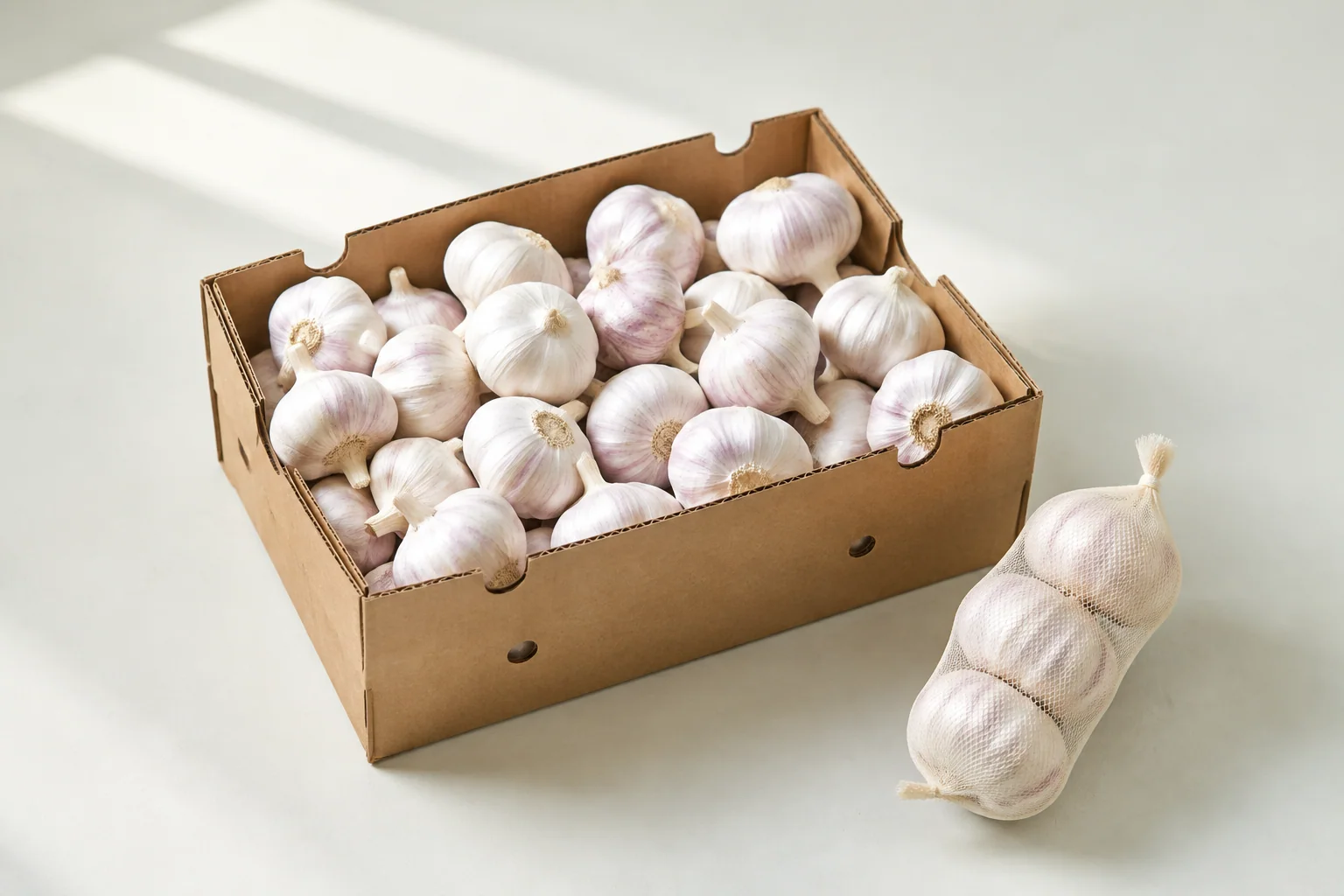 Whole garlic bulbs in a plain carton beside a small mesh pack